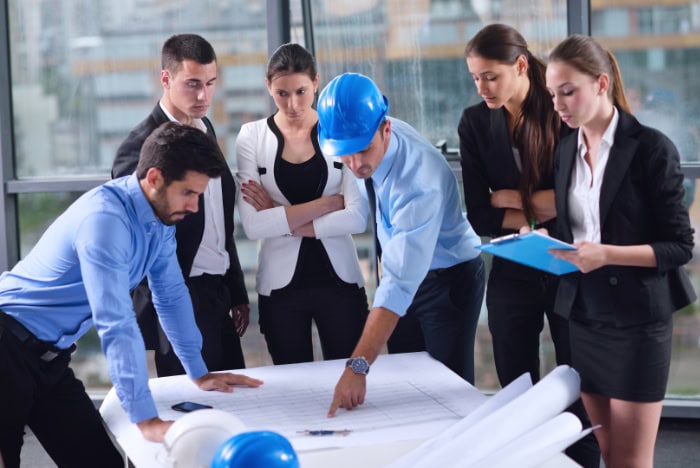 Construction site team reviewing blueprints and technical plans with a project engineer in a modern office setting.